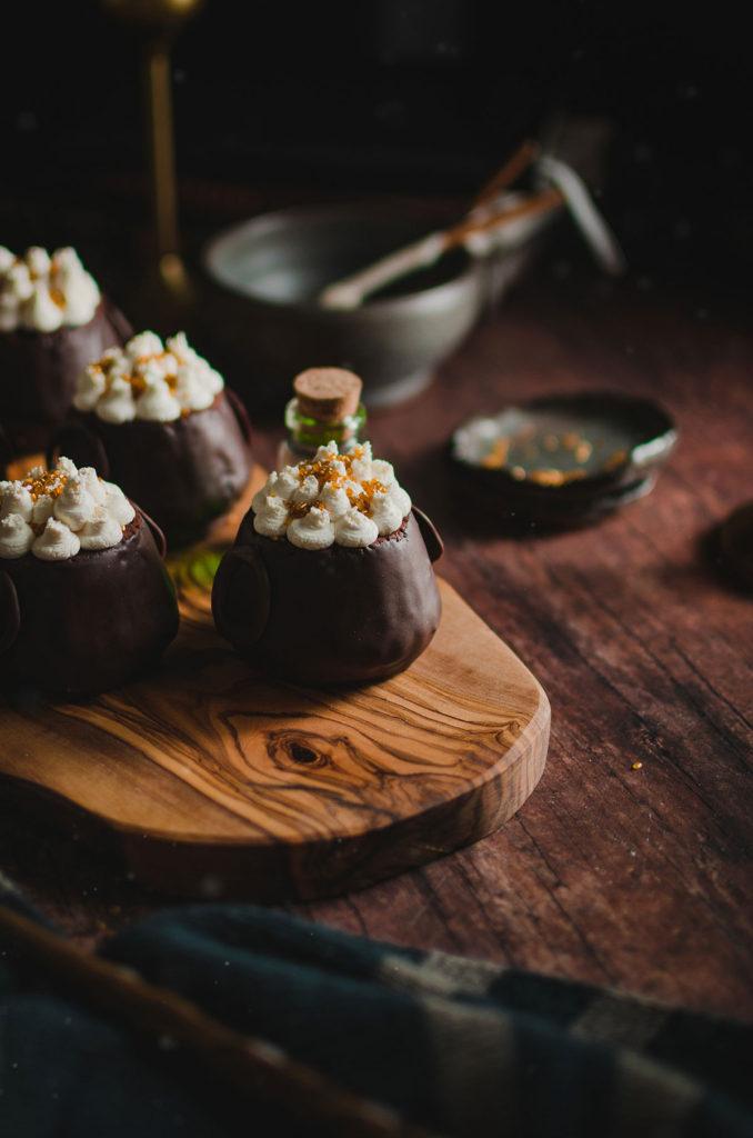 45 degree angle of multiple cauldron cakes set on top of a wooden platter. One cauldron cake in focus, the rest is out of focus.