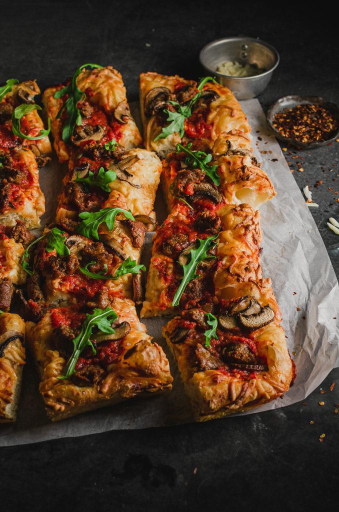 45 degree angle of the vegan Detroit-style pizza, cut into twelve squares, set on top of a piece of parchment paper.
