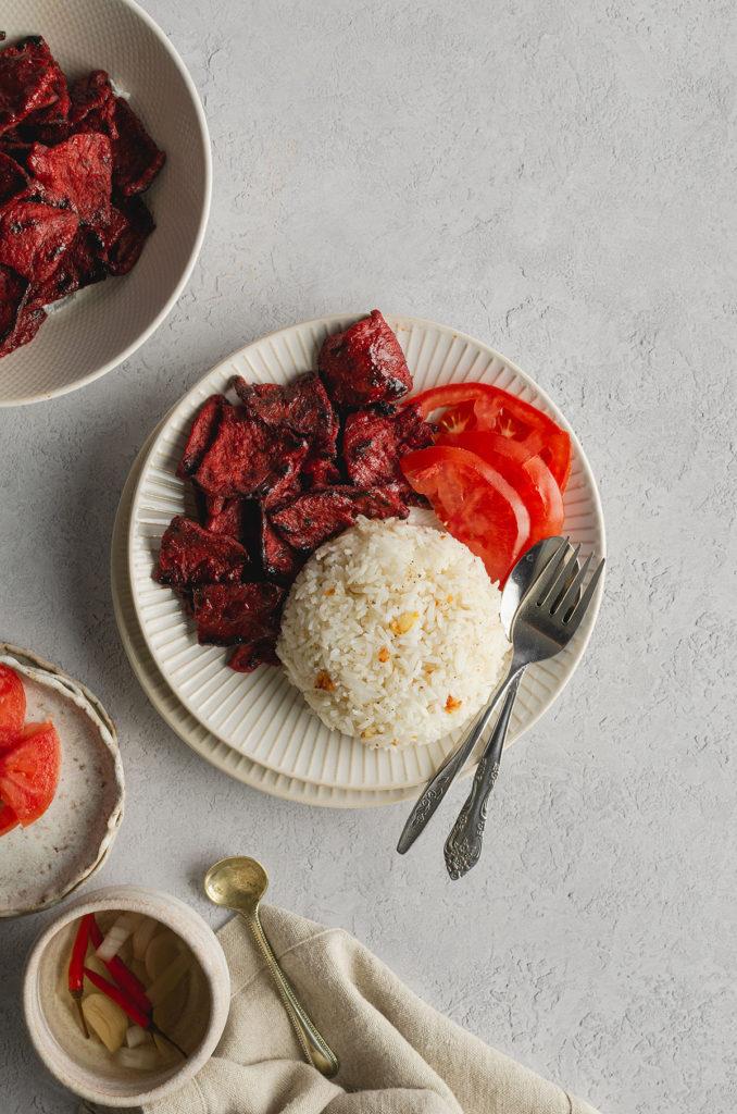 Top view of a plate with vegan filipino tocino, garlic fried rice, and fresh tomatoes