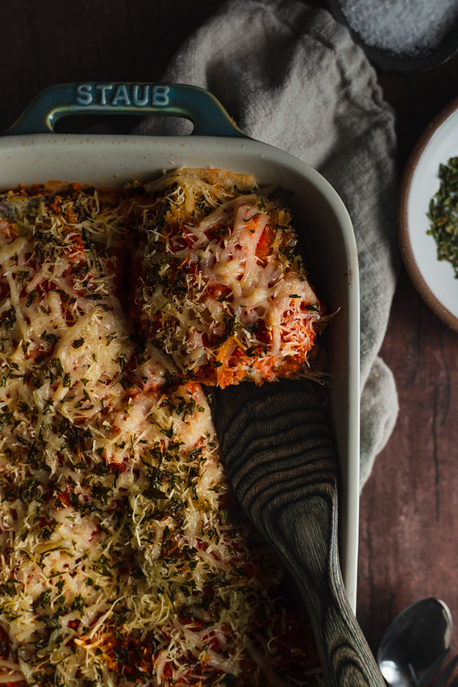Top view and close up of the top right corner of the baking dish with vegan eggplant parmesan being cut into.