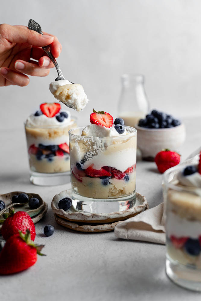 A single of a vegan berry trifle cup and a person taking a scoop out of it.