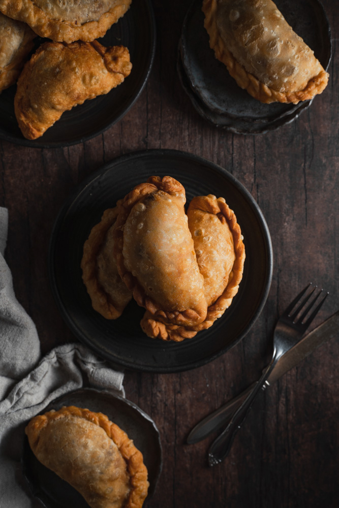 Top view, a plate in the center filled with three vegan filipino empanadas. Surrounded by other plates with empanadas.