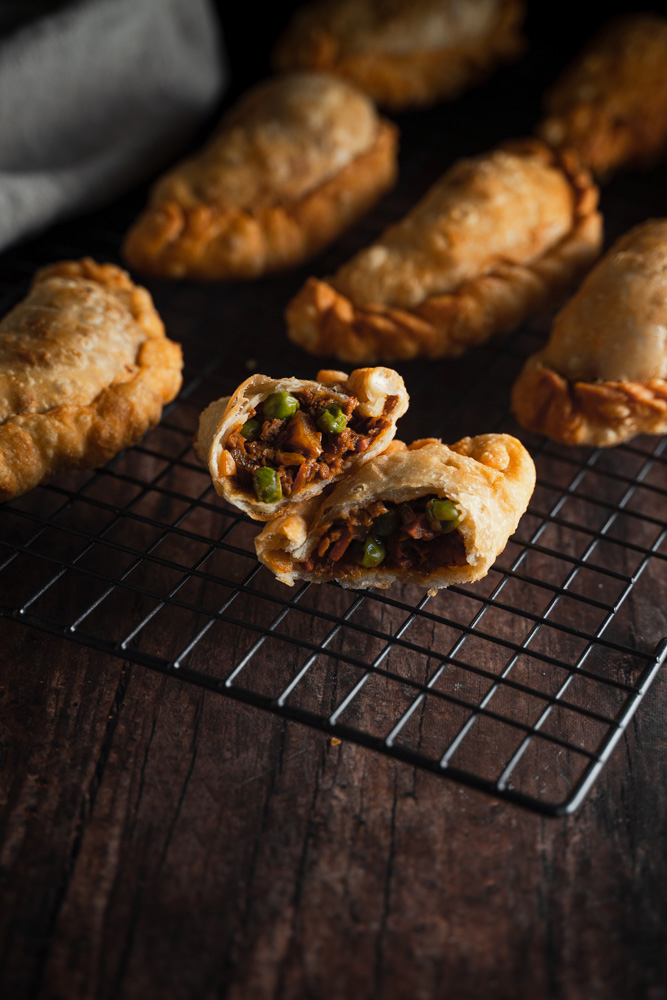 45 degree angle of an open vegan filipino empanada, showing the filling. Layed on top of a wire cooling rack, next to other empanadas.