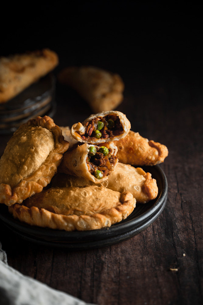 Front angle of a plate of empanadas, and one opened showing the filling.