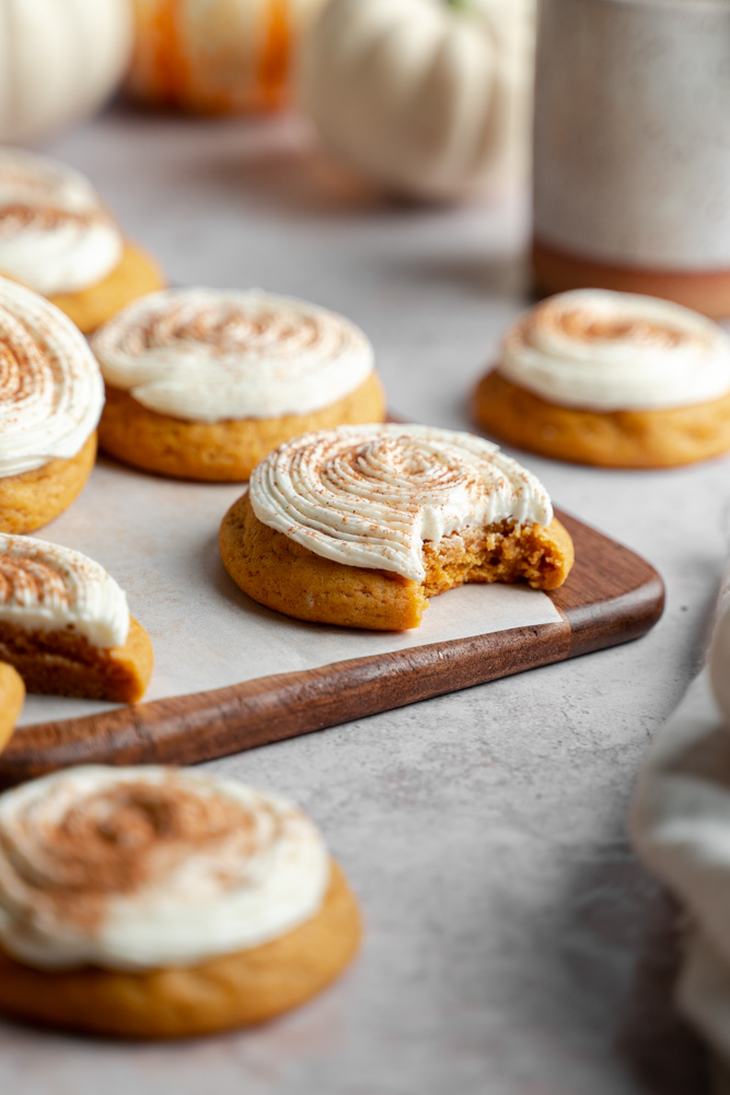 One vegan pumpkin spice cookies  in focus with a bite taken out of it.