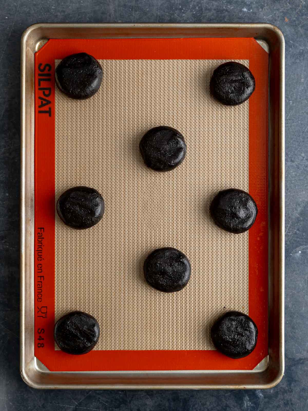 Eight scoops of cookie dough placed on a rimmed baking sheet
