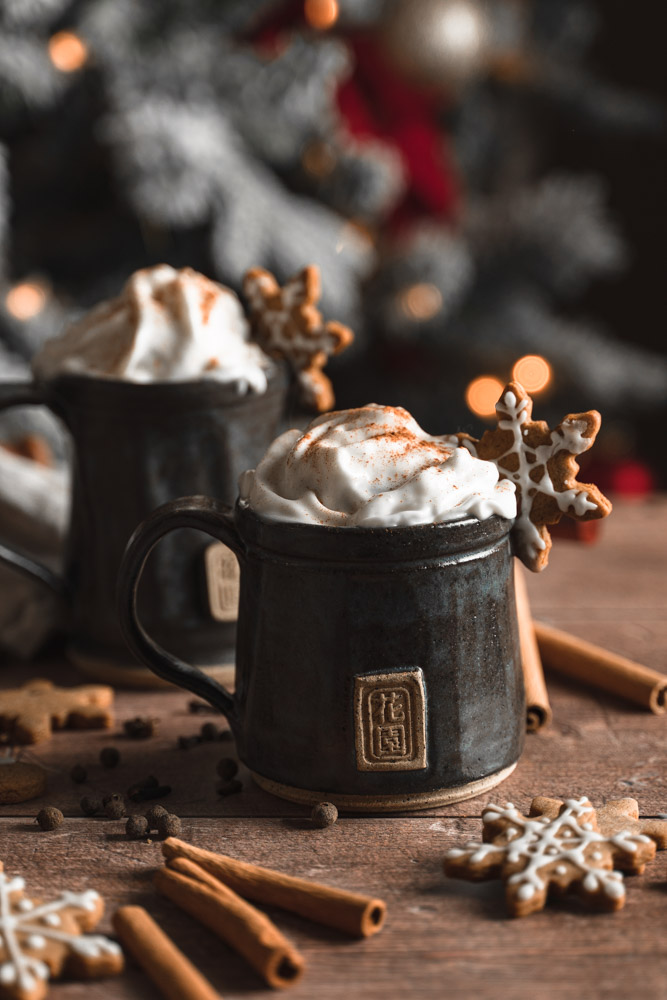 Two cups of gingerbread latte in front of a christmas tree.
