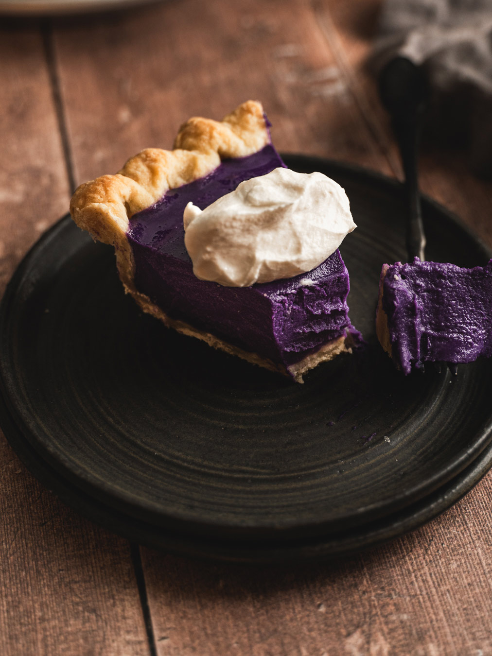 A slice of ube pie with whipped cream on top and a bite taken out of it.