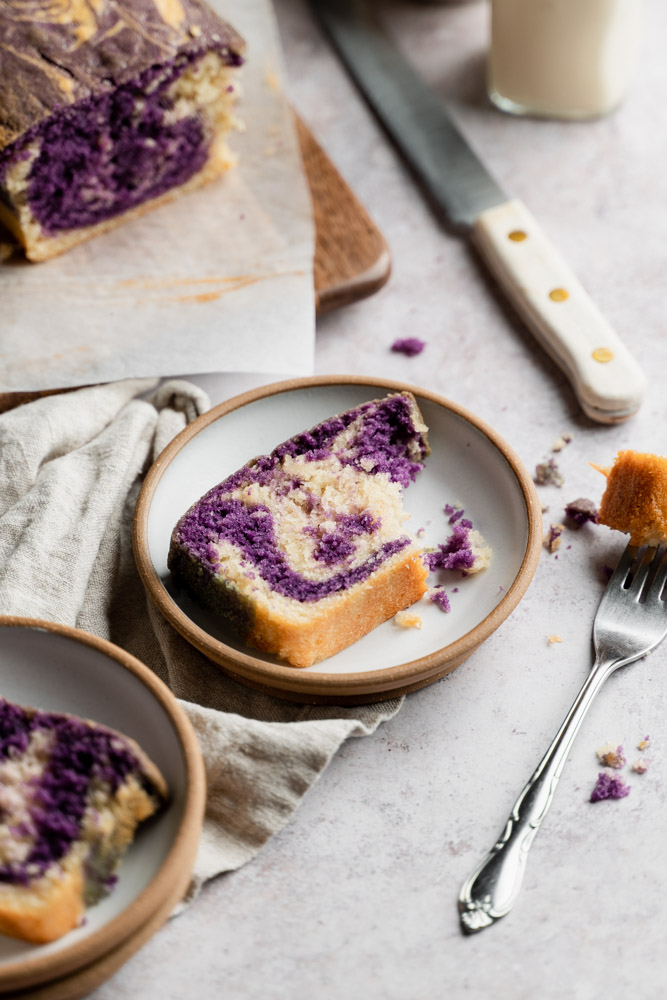 A piece of ube cake on top of a plate with a bite taken out of it.