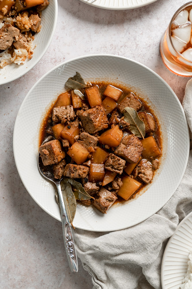 Top view of a bowl of tofu adobo with diced potatoes, sauce, and bay leaves.