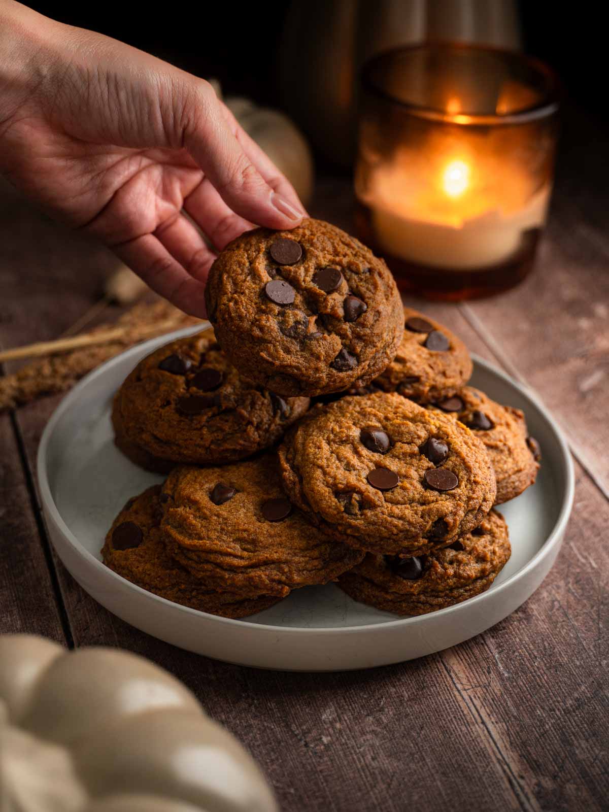 A plate of vegan pumpkin chocolate chip cookies and a hand taking a piece.
