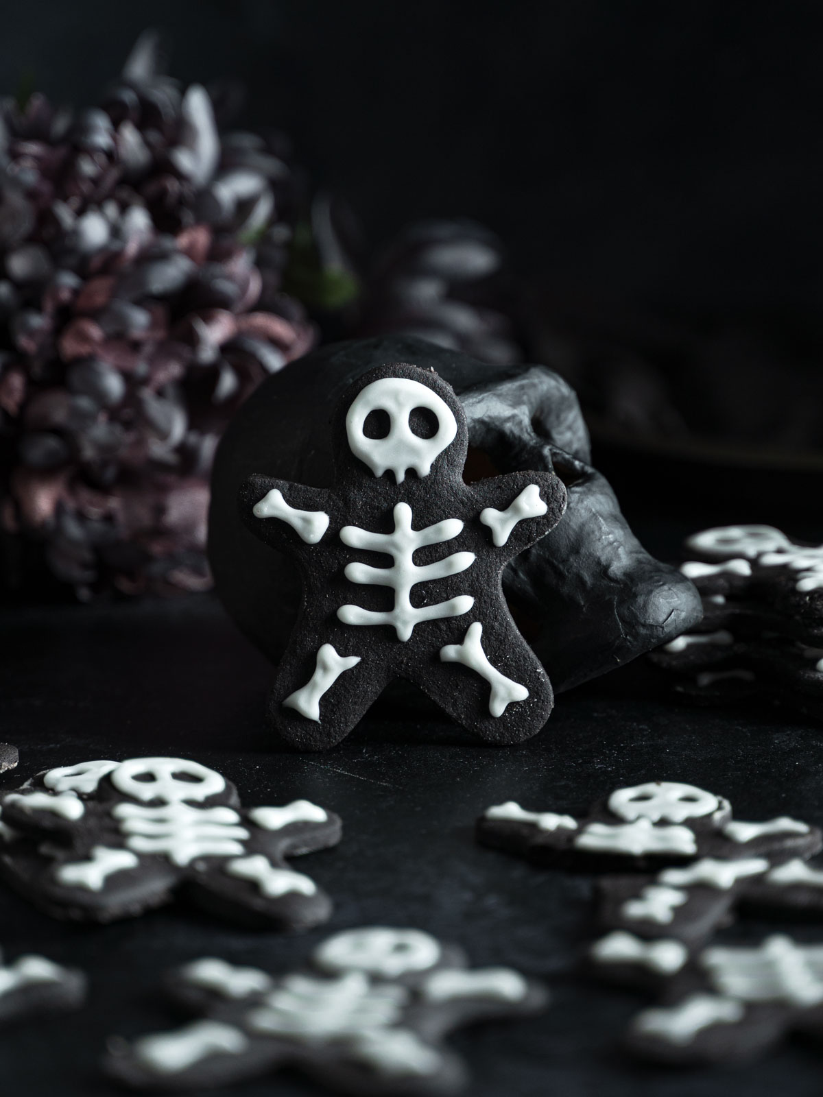 A single vegan skeleton cookie standing against a black prop skull.
