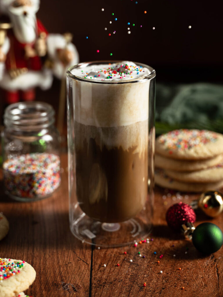 A glass of the vegan iced sugar cookie latte with sprinkles flying over the top.
