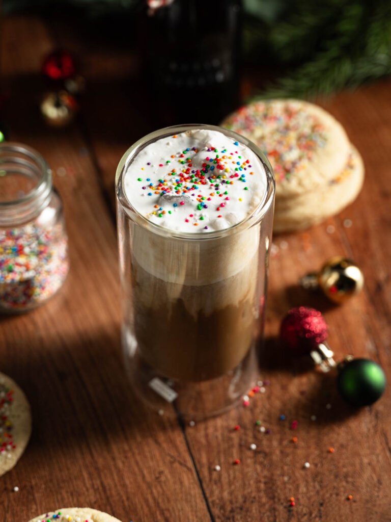 Tall glass of vegan iced sugar cookie latte with sprinkles on top.