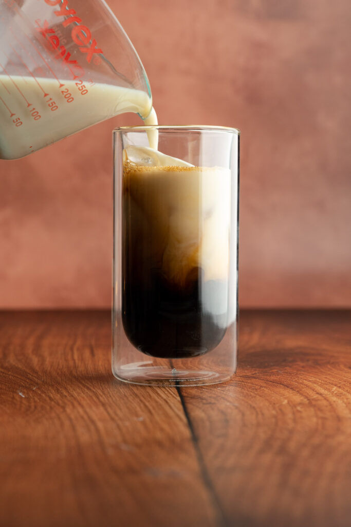 Tall glass with a glass pitcher with oat milk being poured in.