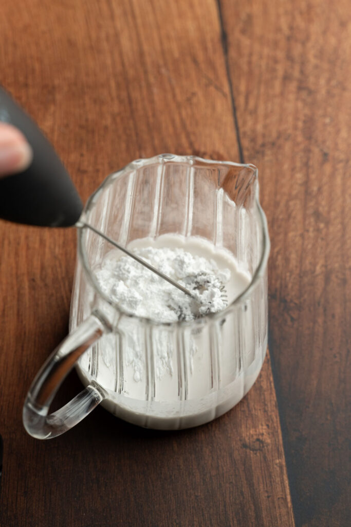 Small glass pitcher with sweet cream ingredients, and a frothing wand.