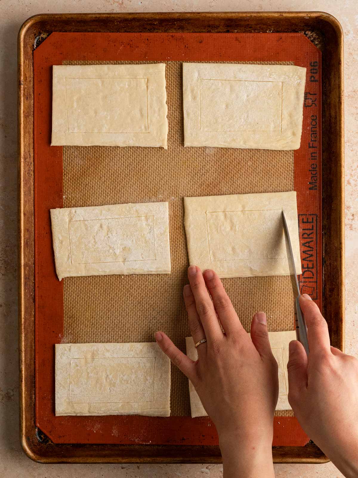 Six small rectangle puff pastry being scored with a paring knife.