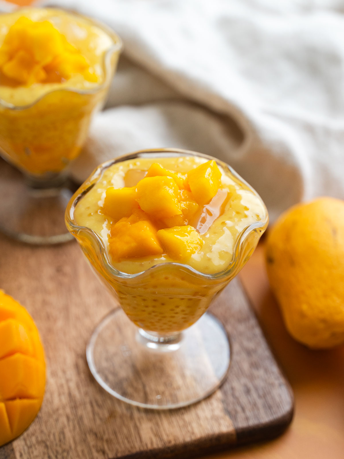 A sundae glass full of vegan mango sago with chopped mangoes on top.