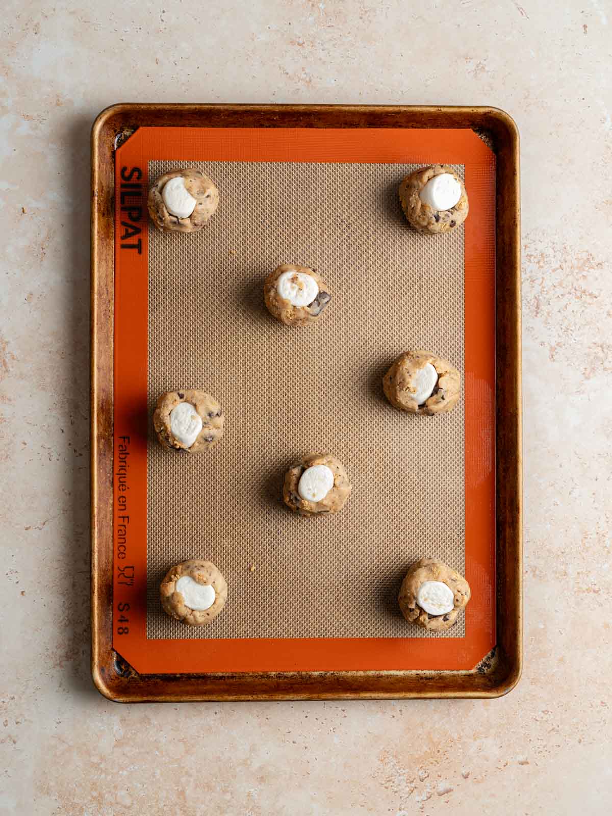 Marshmallow filled cookie dough balls placed on a rimmed baking sheet.