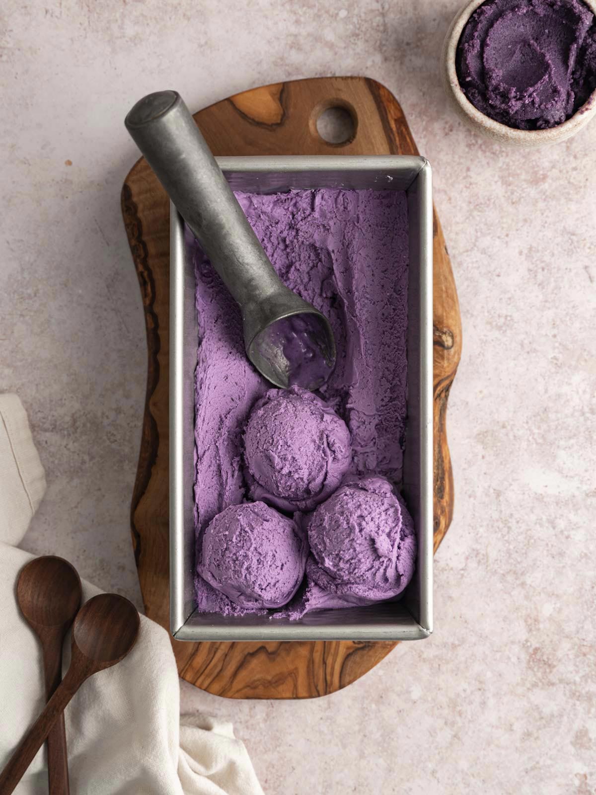 Purple ice cream in a metal container, with three scoops.