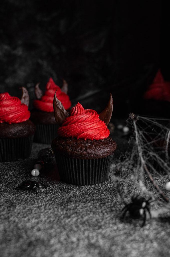 A single halloween devil cupcake in the center, with three more in the back. Surrounded with spider webs.