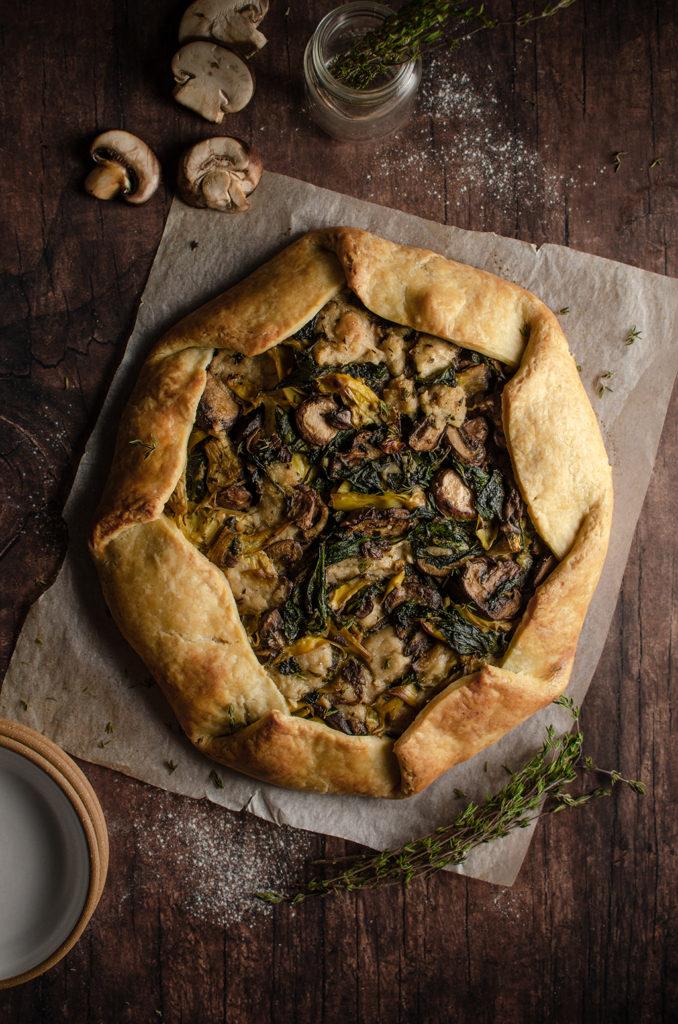 Top view of a whole vegan mushroom and spinach artichoke galette. 