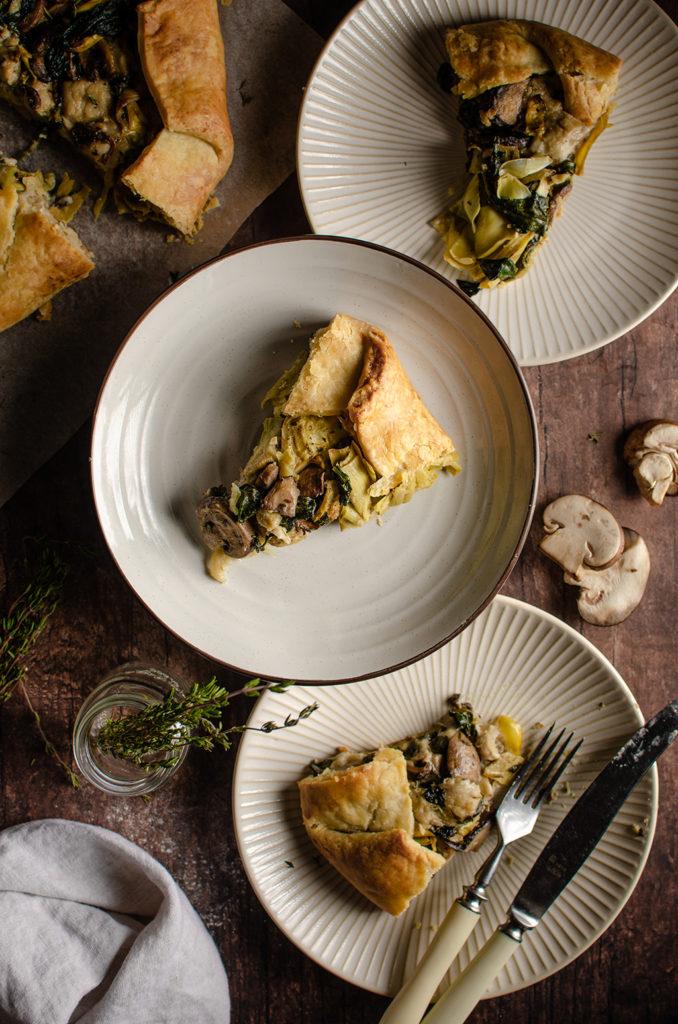 Top view of three vegan mushroom and spinach artichoke galette slices on plates.