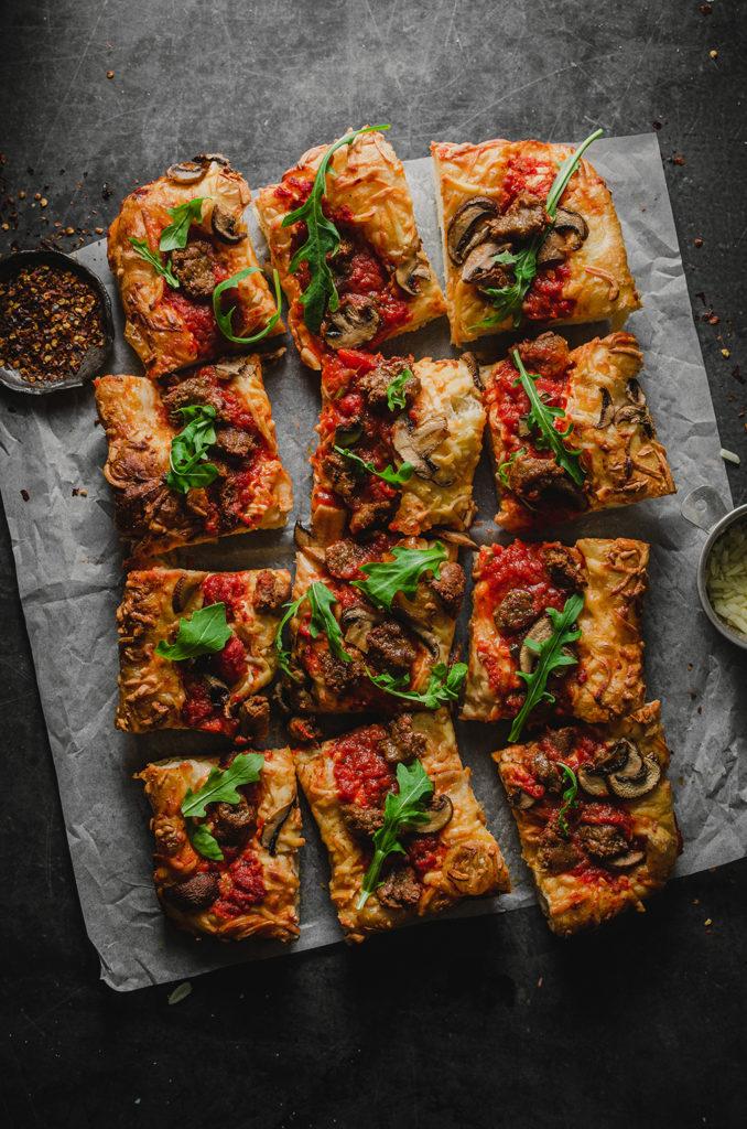 Top view of the vegan Detroit-style pizza, cut into twelve squares, set on top of a piece of parchment paper. 