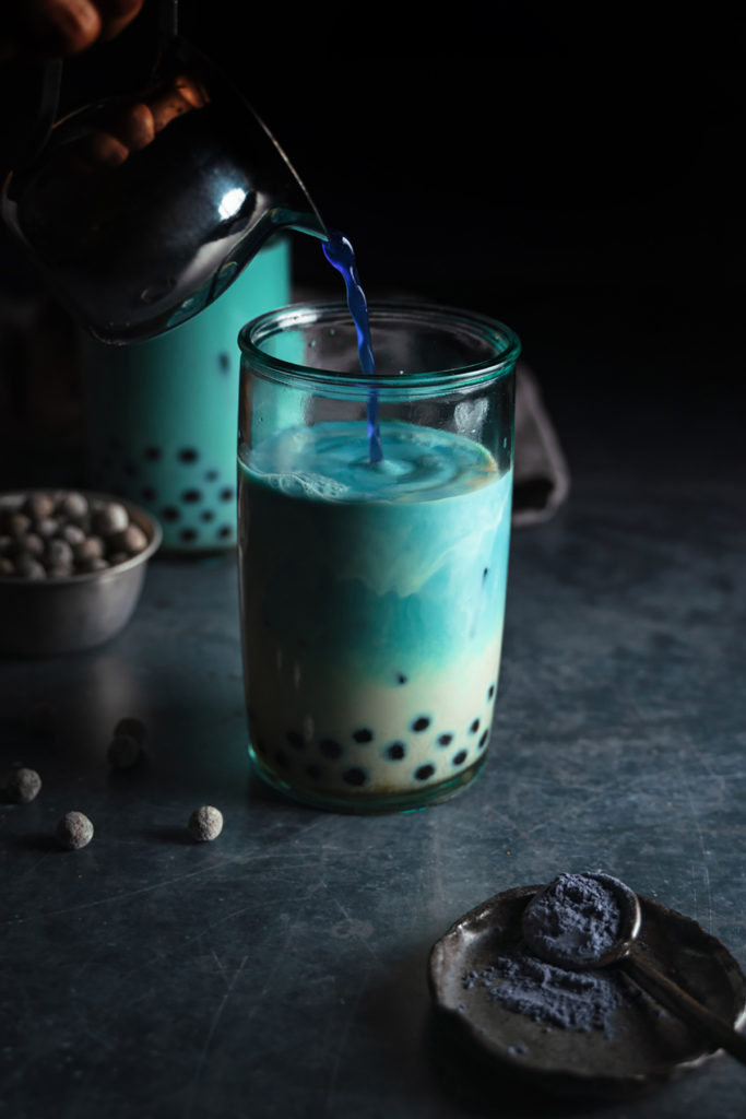Front view of a glass of milk and tapioca pearls. Butterfly pea tea poured into the cup and changing the color of the milk blue.