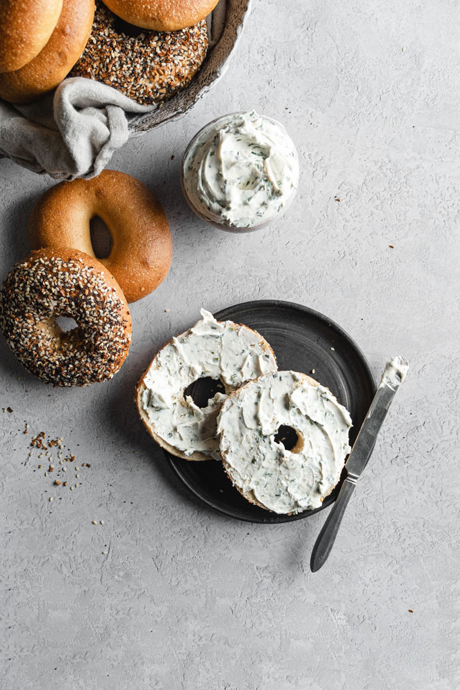 A plate of a New York-Style Bagel, cut in half with cream cheese spread on it.