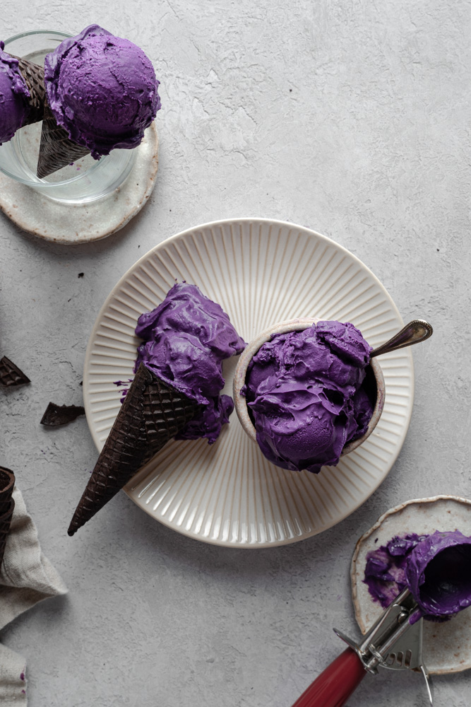 vegan ube ice cream in a bowl and in a cone, placed on top of a plate.
