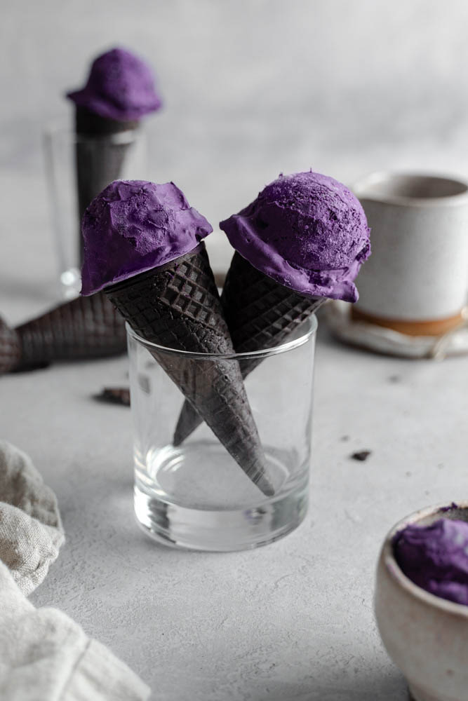 Two vegan ube ice cream in oreo cones, standing in a glass cup.