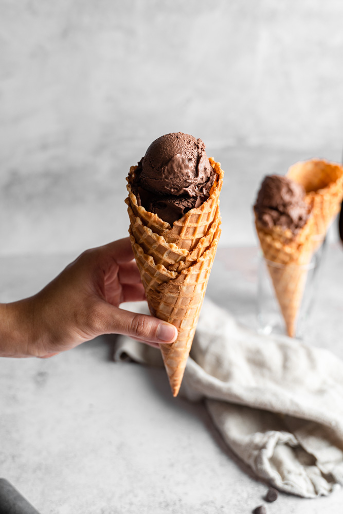 Hand holding a cone of vegan chocolate ice cream.