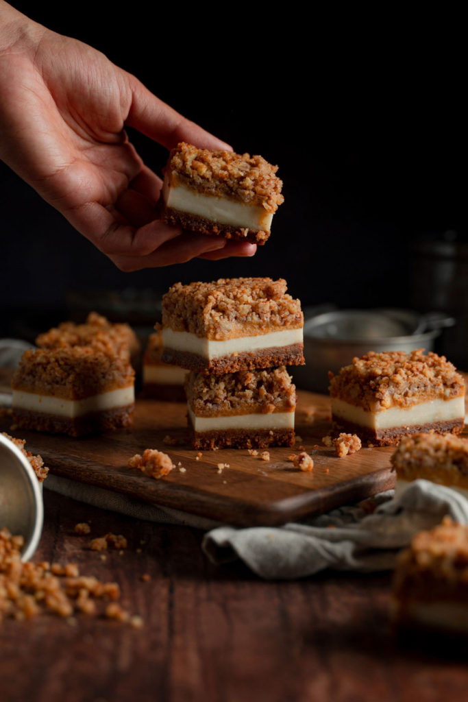 Three stacked vegan pumpkin cheesecake bars. A hand reaching out on to the top cheesecake bar.