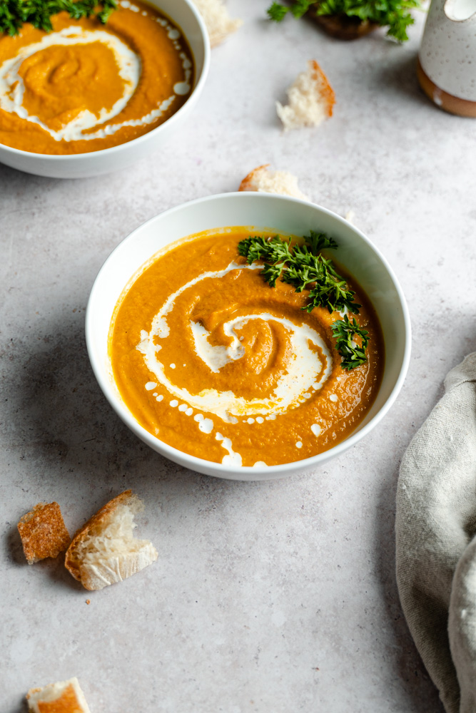 A single bowl of vegan savory pumpkin soup with pieces of bread around it.
