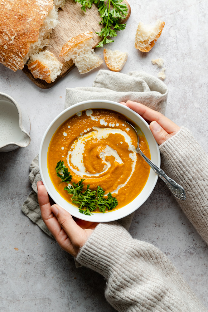 Hands holding a bowl of vegan savory pumpkin soup.