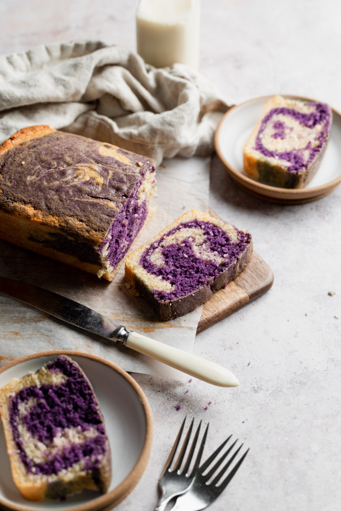 A loaf shaped vegan ube marble cake cut into 3 slices, set ontop of a wooden board.