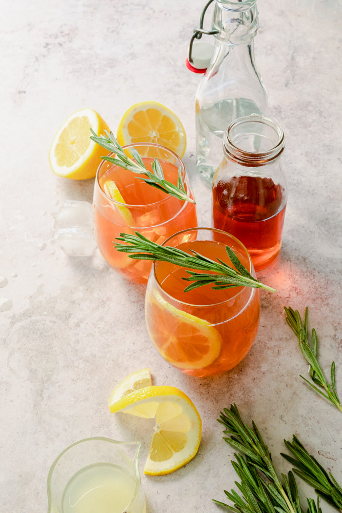 Two glasses of peach tea sparkling mocktail with a slice of lemon inside and a sprig of rosemary on top.