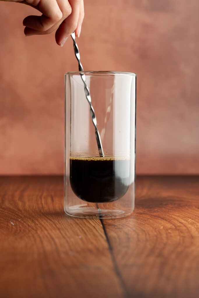Tall glass with espresso and a stirrer.