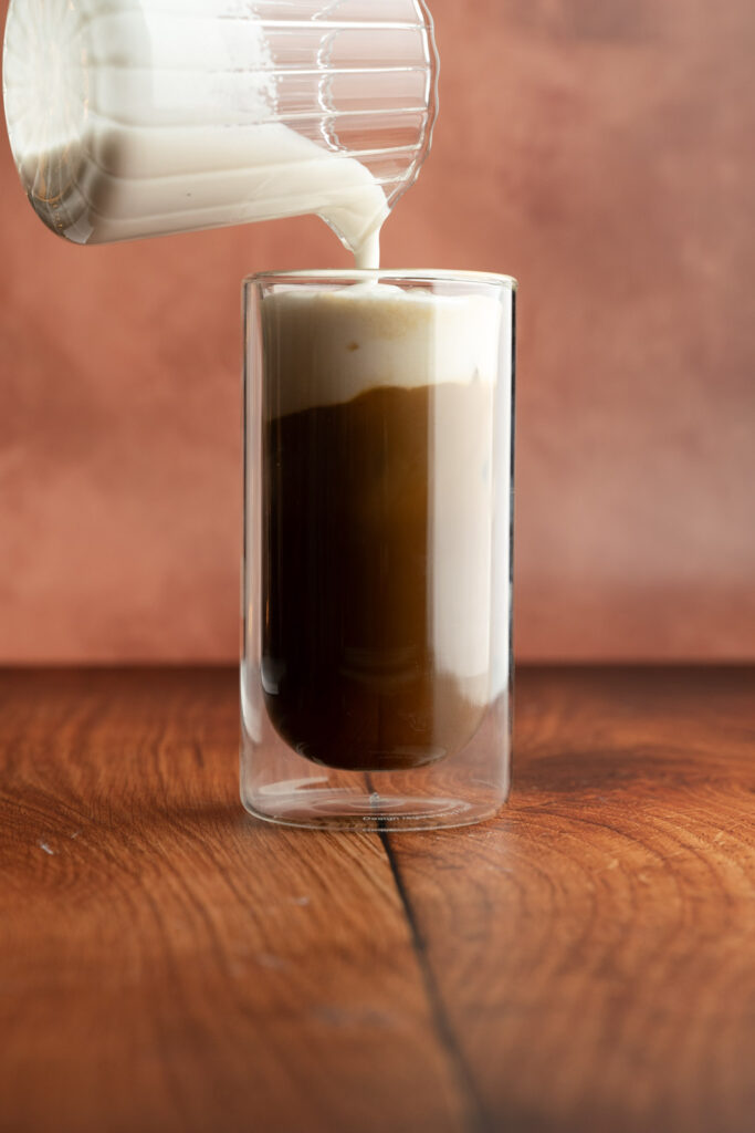 Tall glass with a small pitcher of sweet cream being poured on top of the drink.