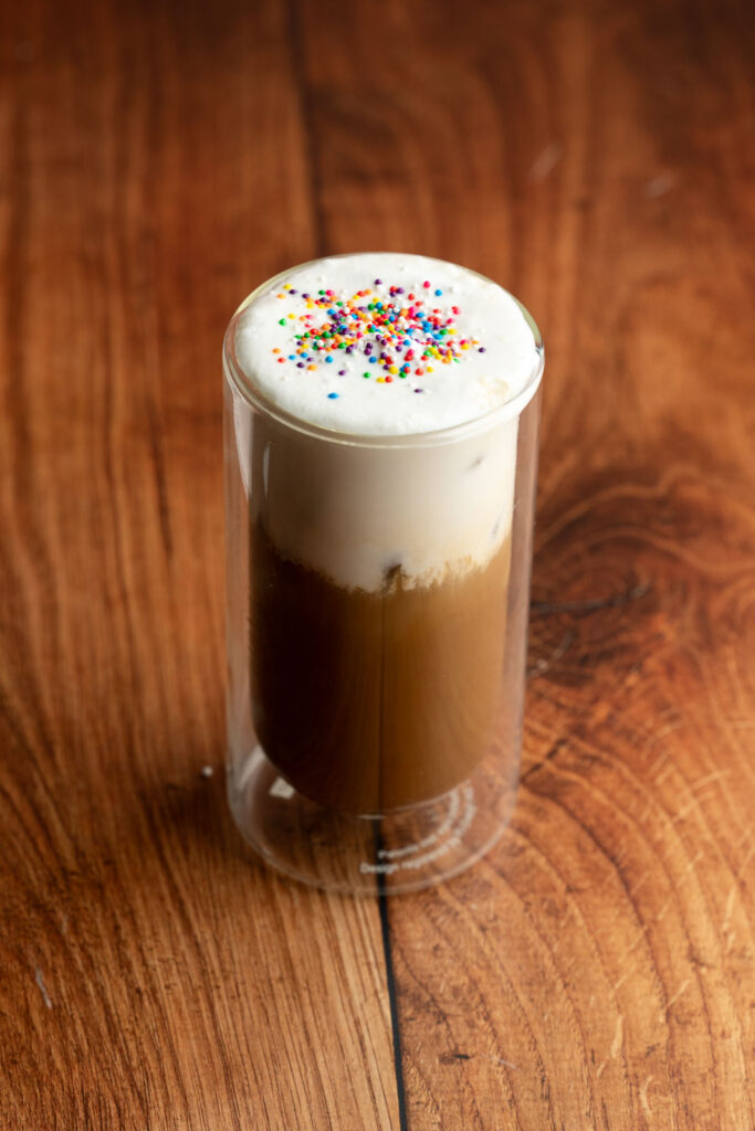 Glass with vegan iced sugar cookie latte with sprinkles on top.