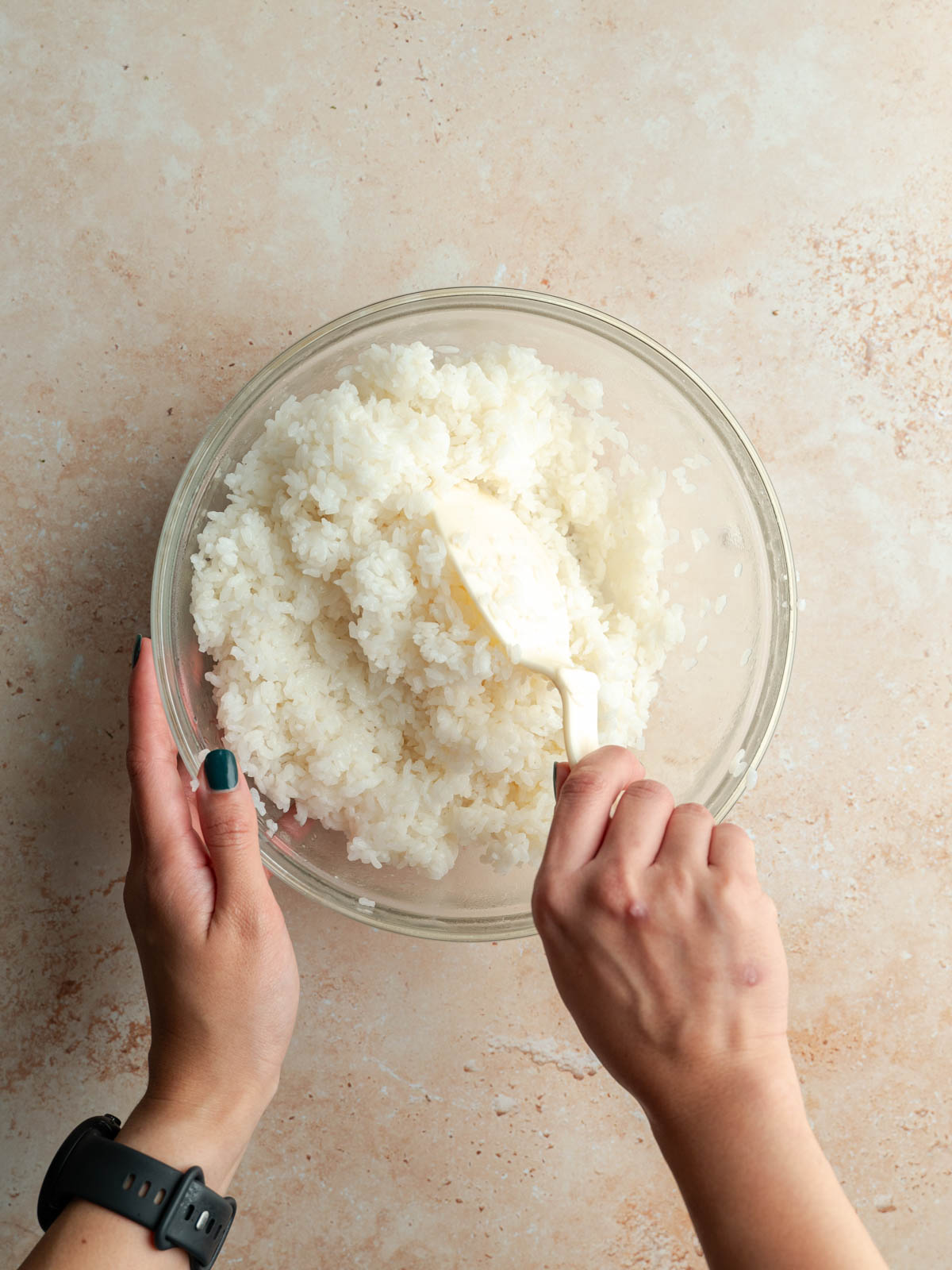 Mixing the sushi rice with rice vinegar mixture in a bowl.