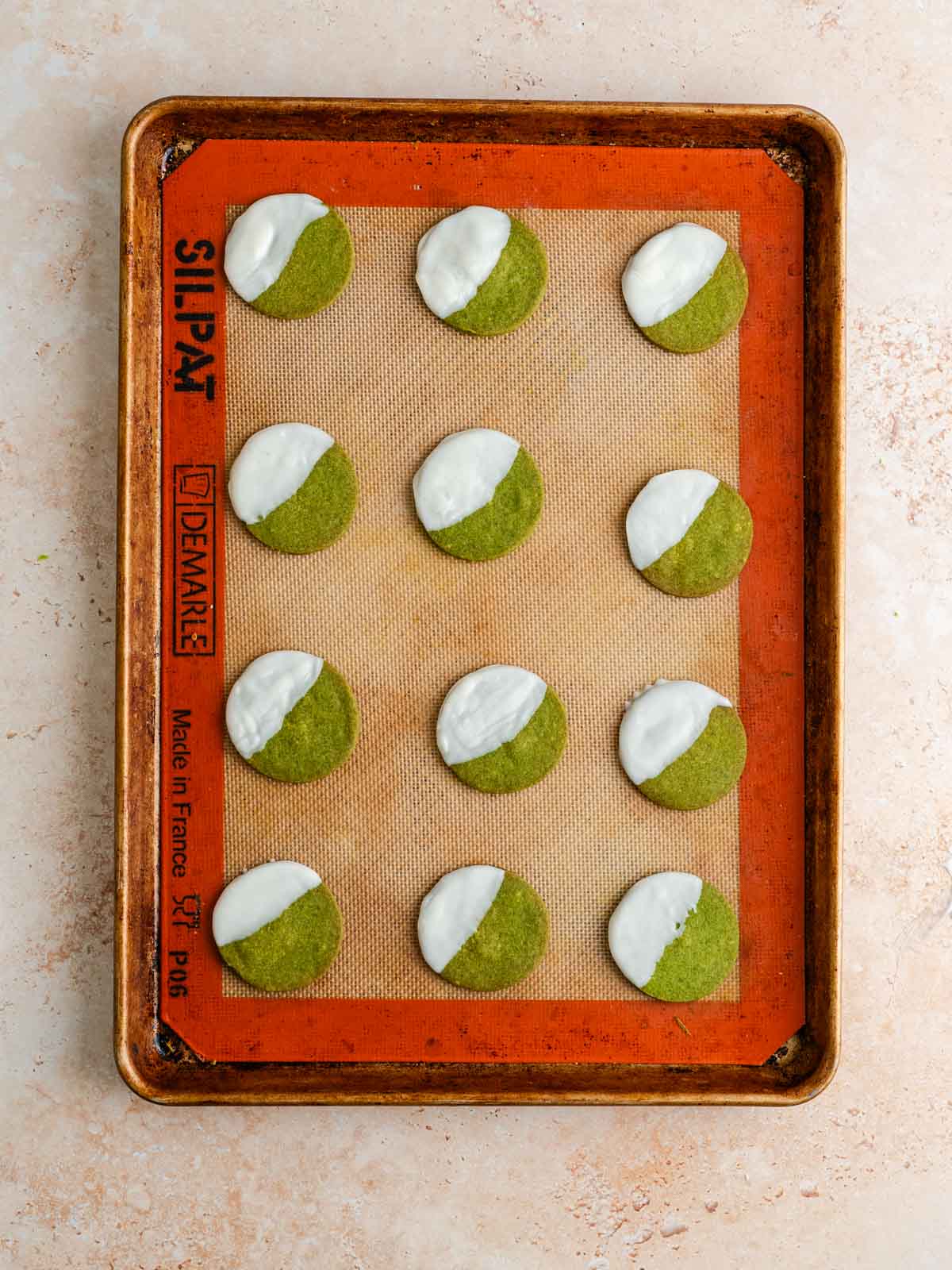 Vegan matcha shortbread cookies dipped in white chocolate on a baking sheet.