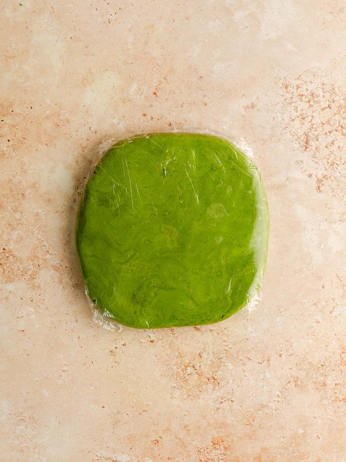 Matcha cookie dough flattened and wrapped in plastic.