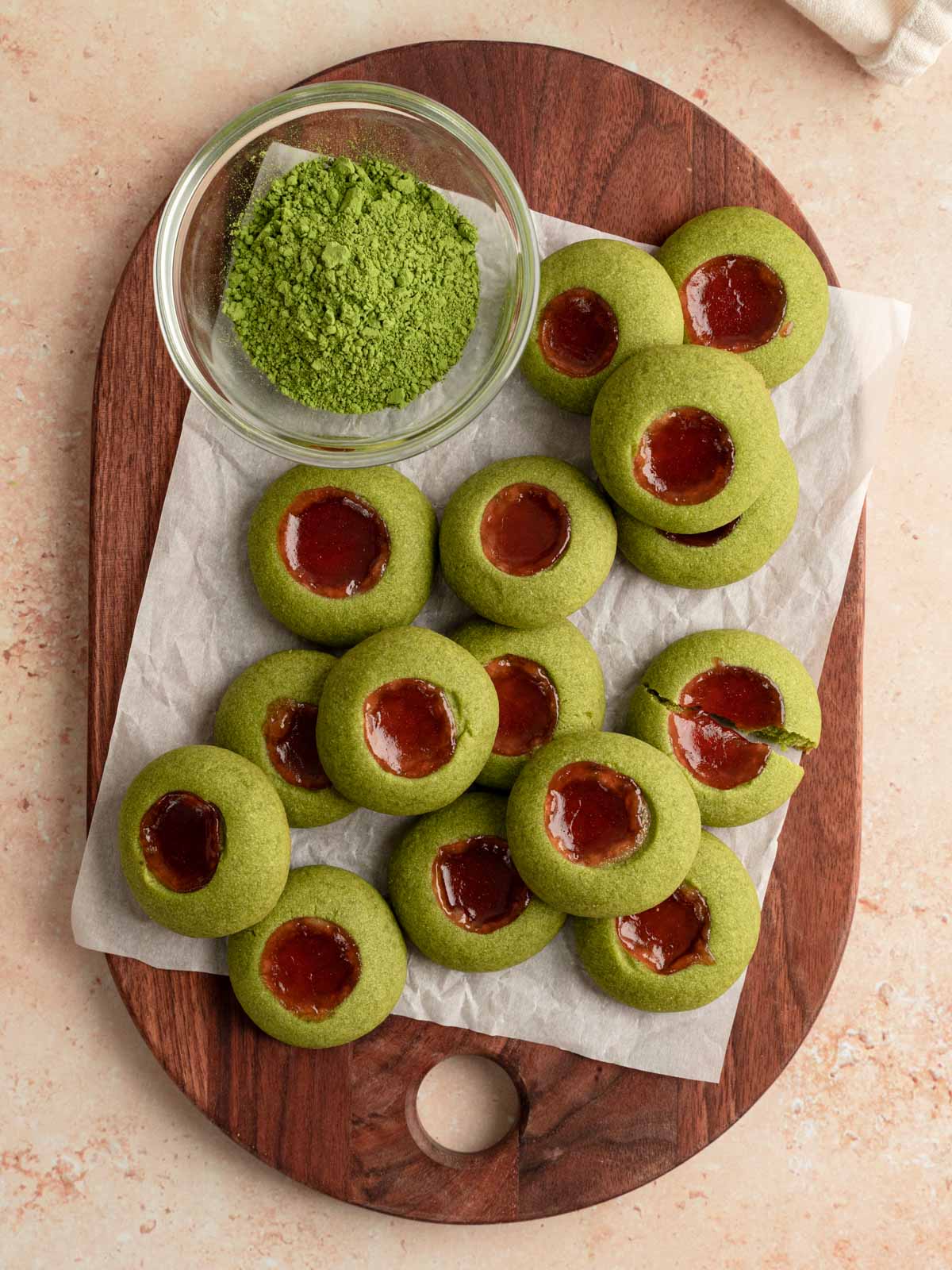 A wooden board with vegan matcha thumbprint cookies laid out on top.